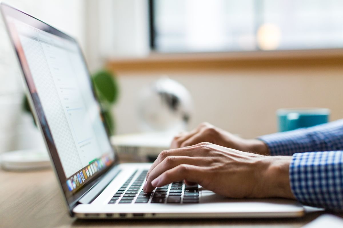 Close-up of an adult typing on a laptop in a bright, modern office
