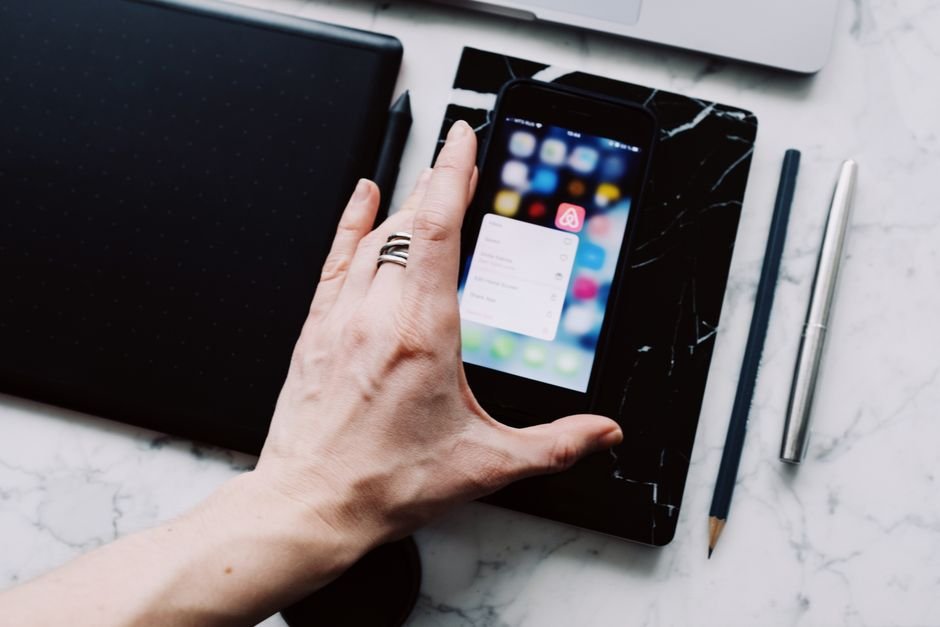 Person browsing a smartphone on a white marble desk surrounded by everyday gadgets
